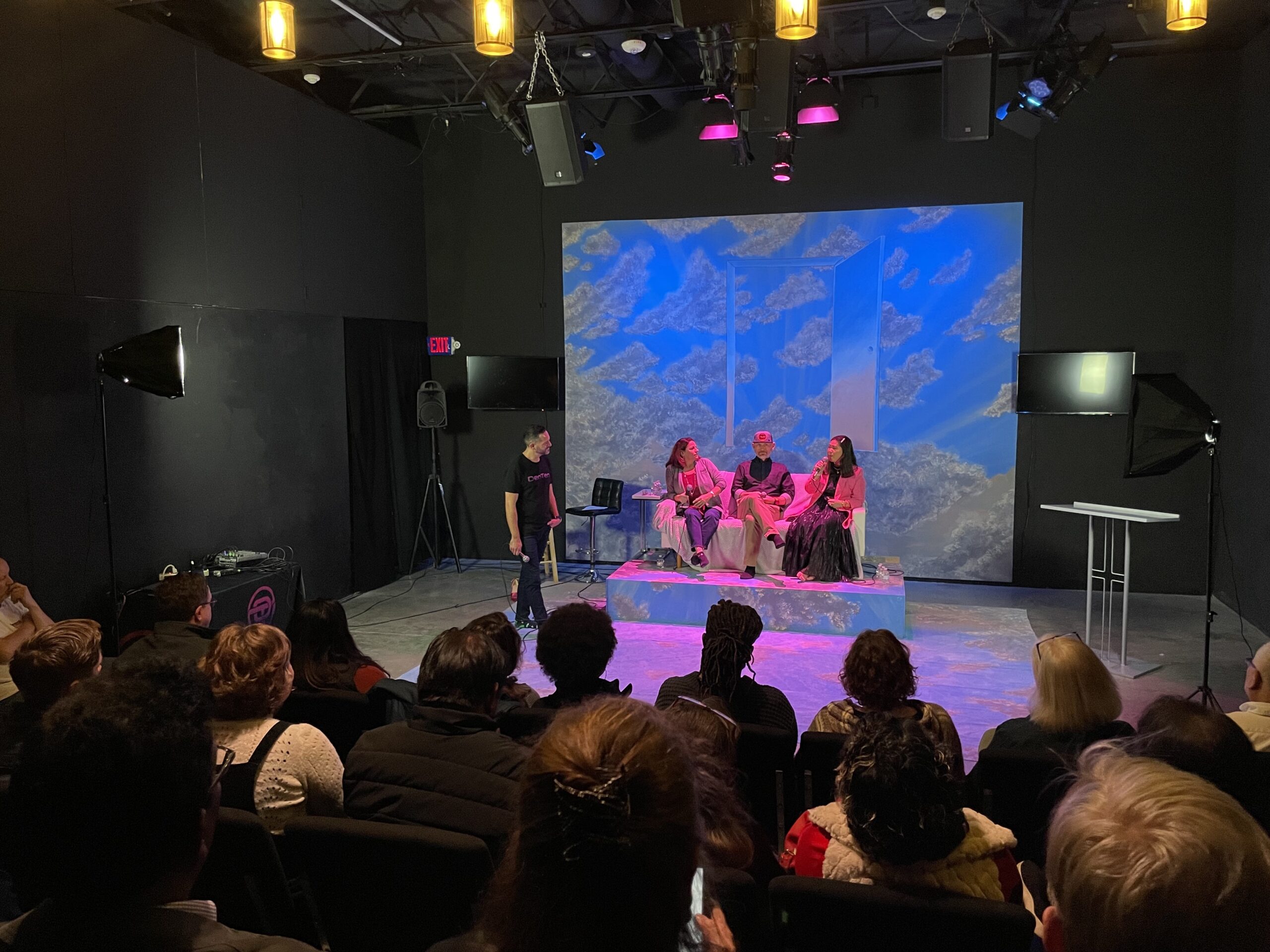 Michael hosting a panel os speakers at an event in a dark room with a large audience