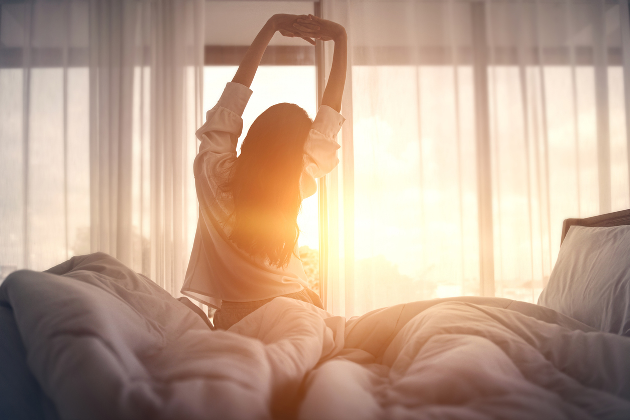 Happy woman stretching in bed after waking up. Happy young girl greets good day.