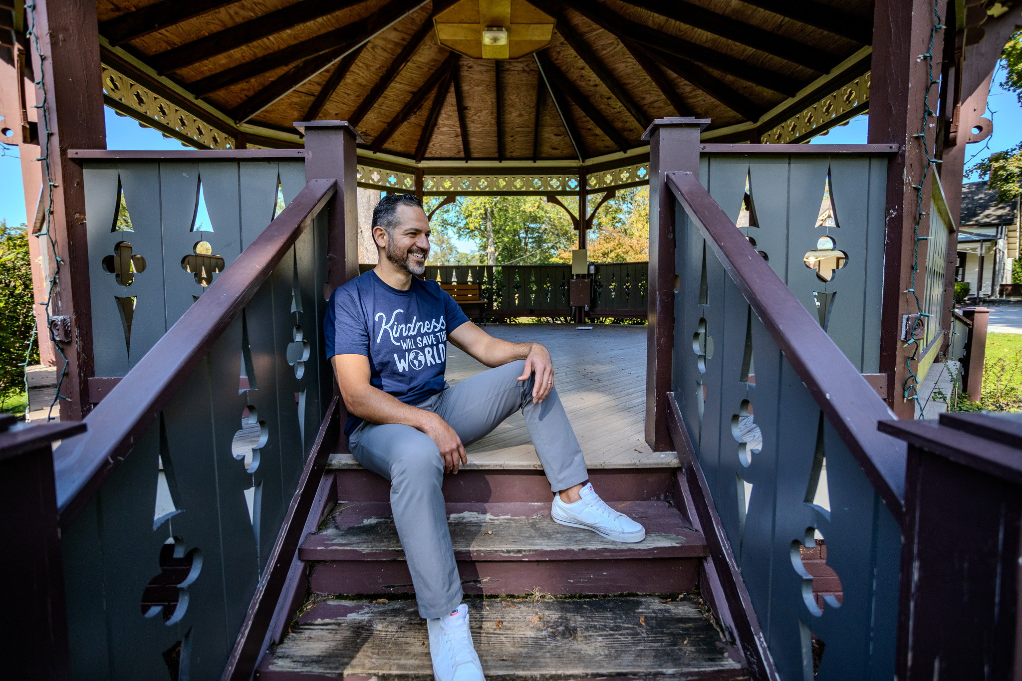 Michael Esposito sitting on the steps of a gazebo in Wappingers Falls wearing a blue shirt that says Kindness wil save the world